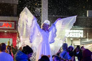 a person dress as an angel stands illuminated under falling snow