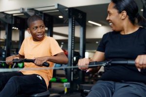 A boy and a woman use rowing machines
