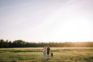 Two people and a child stand admiring a sunset