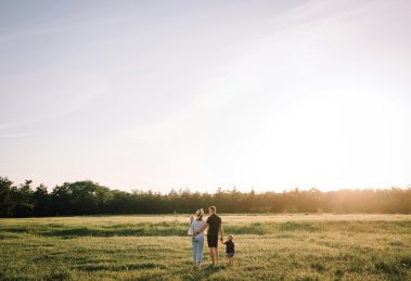 Two people and a child stand admiring a sunset