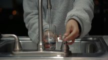 a person holds a glass under a running water tap
