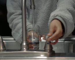 a person holds a glass under a running water tap