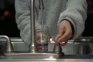 a person holds a glass under a running water tap