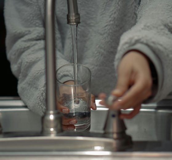 a person holds a glass under a running water tap